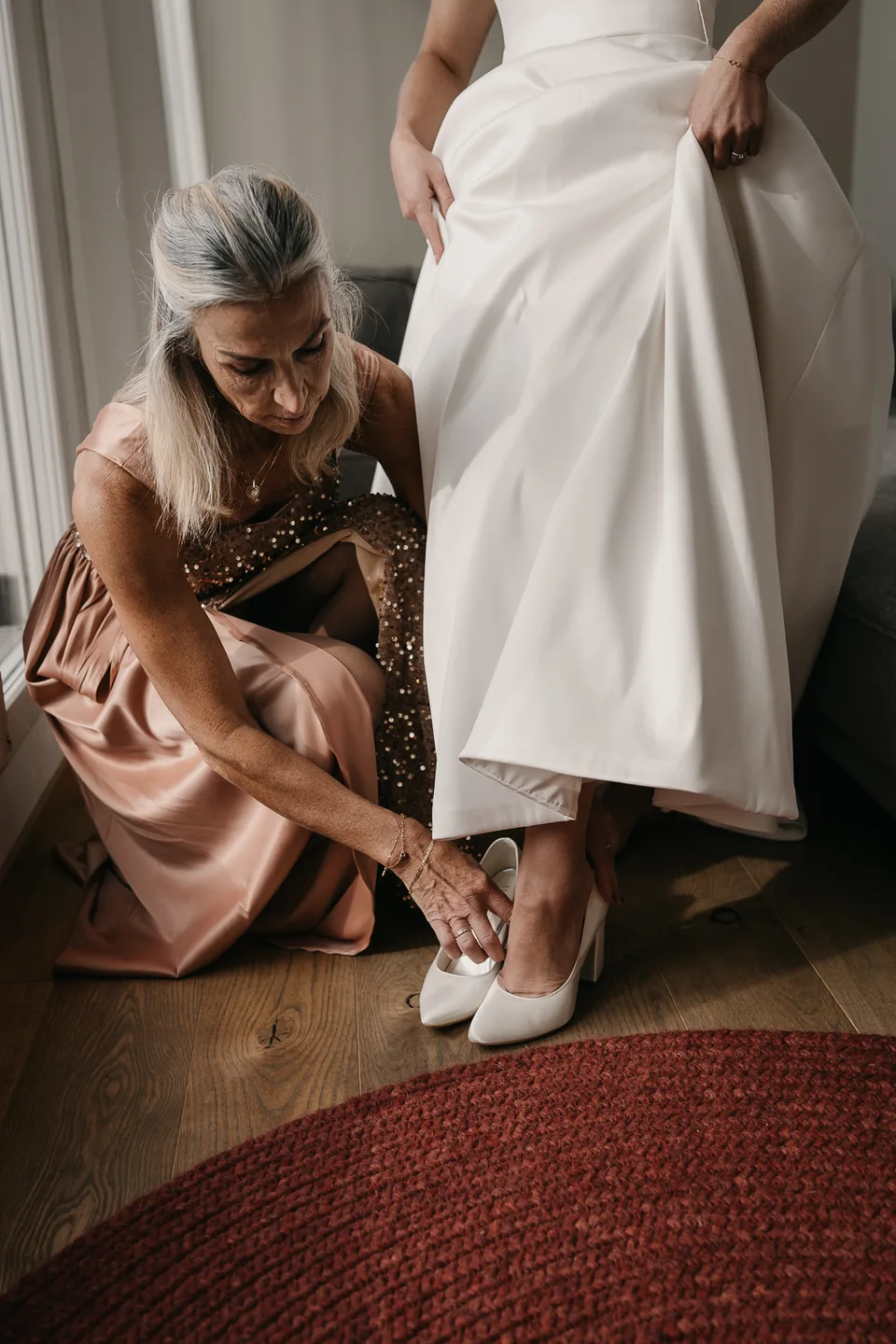 Eine Freundin hilft der Braut beim Anziehen der Brautschuhe