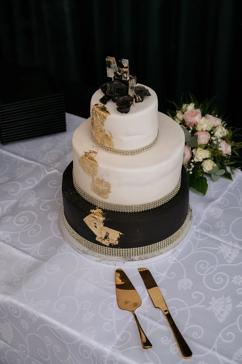 Dreistöckige Hochzeitstorte mit goldenen Details, davor liegt das Tortenbesteck